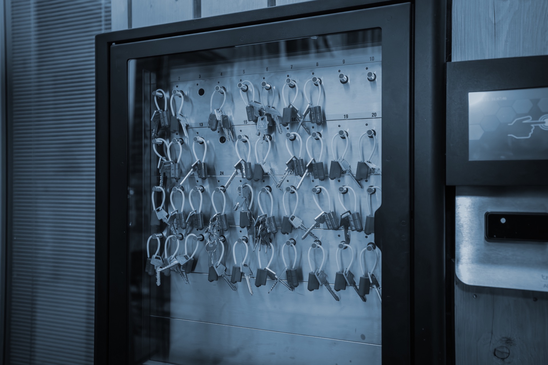 Key management system with multiple keys attached to green tags in a secure glass cabinet, featuring a digital access panel on the side.